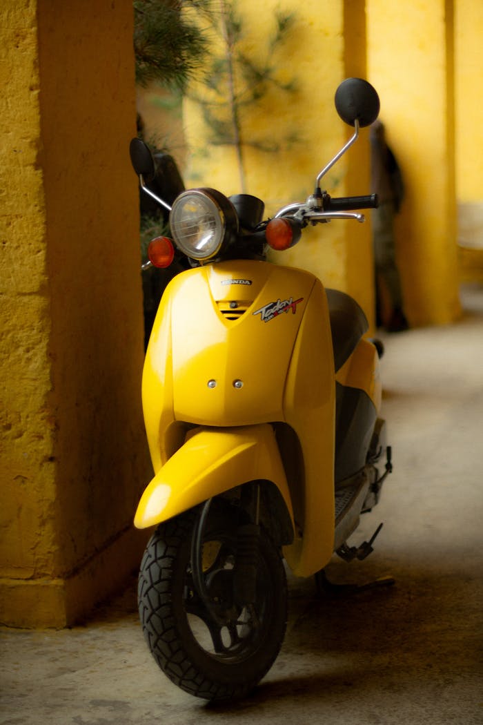 Retro-style yellow scooter parked near indoor pillars. Warm lighting and vintage vibe.